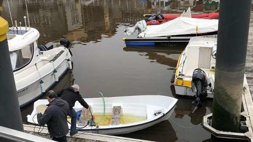 Dos personas achican agua de un bote en Llanes.