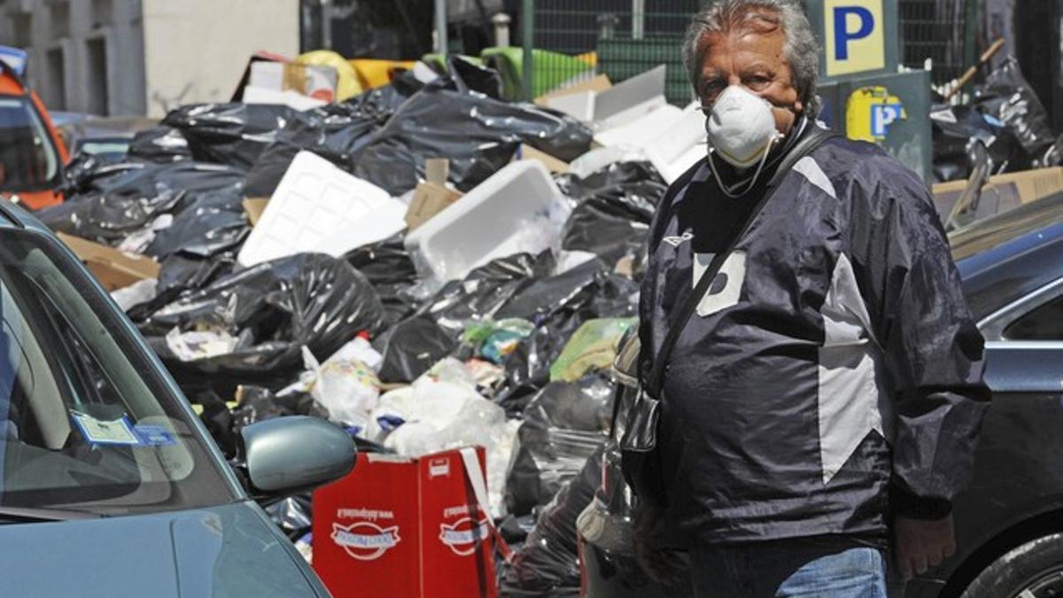 Un vigilante de un párking se protege del mal olor con una mascarilla, junto a un montón de basura sin recoger, en Nápoles.