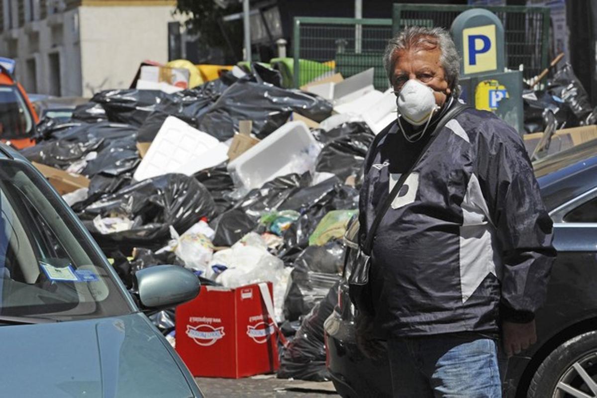 Un vigilant d’un pàrquing es protegeix de la pudor amb una mascareta, al costat d’un munt d’escombraries sense recollir, a Nàpols.