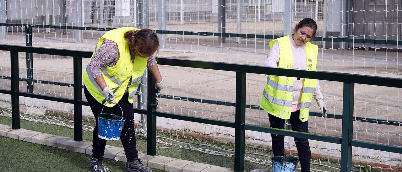 Dos operarias restauran una de las vallas del estadio municipal de fútbol.