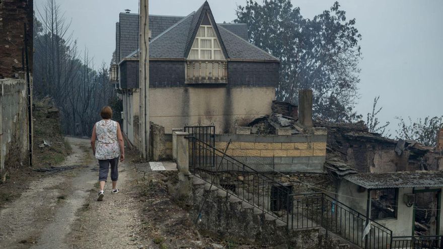 Una mujer camina en Alixo entre las casas calcinadas y alguna que sobrevivió a las llamas. | // BRAIS LORENZO