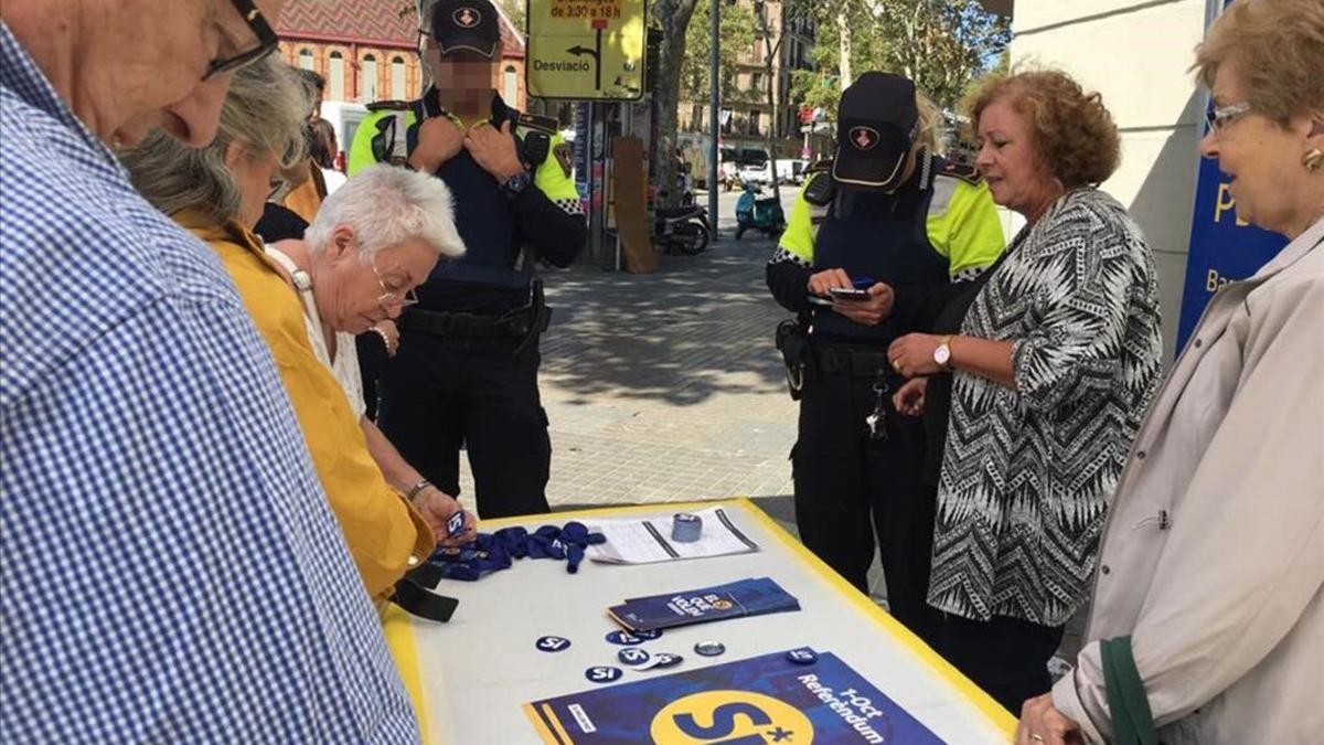 Dos guardias urbanos identifican a los miembros de una parada informativa sobre el referéndum, este sábado en Barcelona.