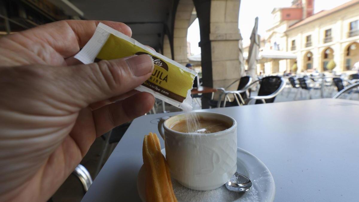 Una persona echa un sobre de azúcar en un café, en la plaza del Ayuntamiento de Avilés
