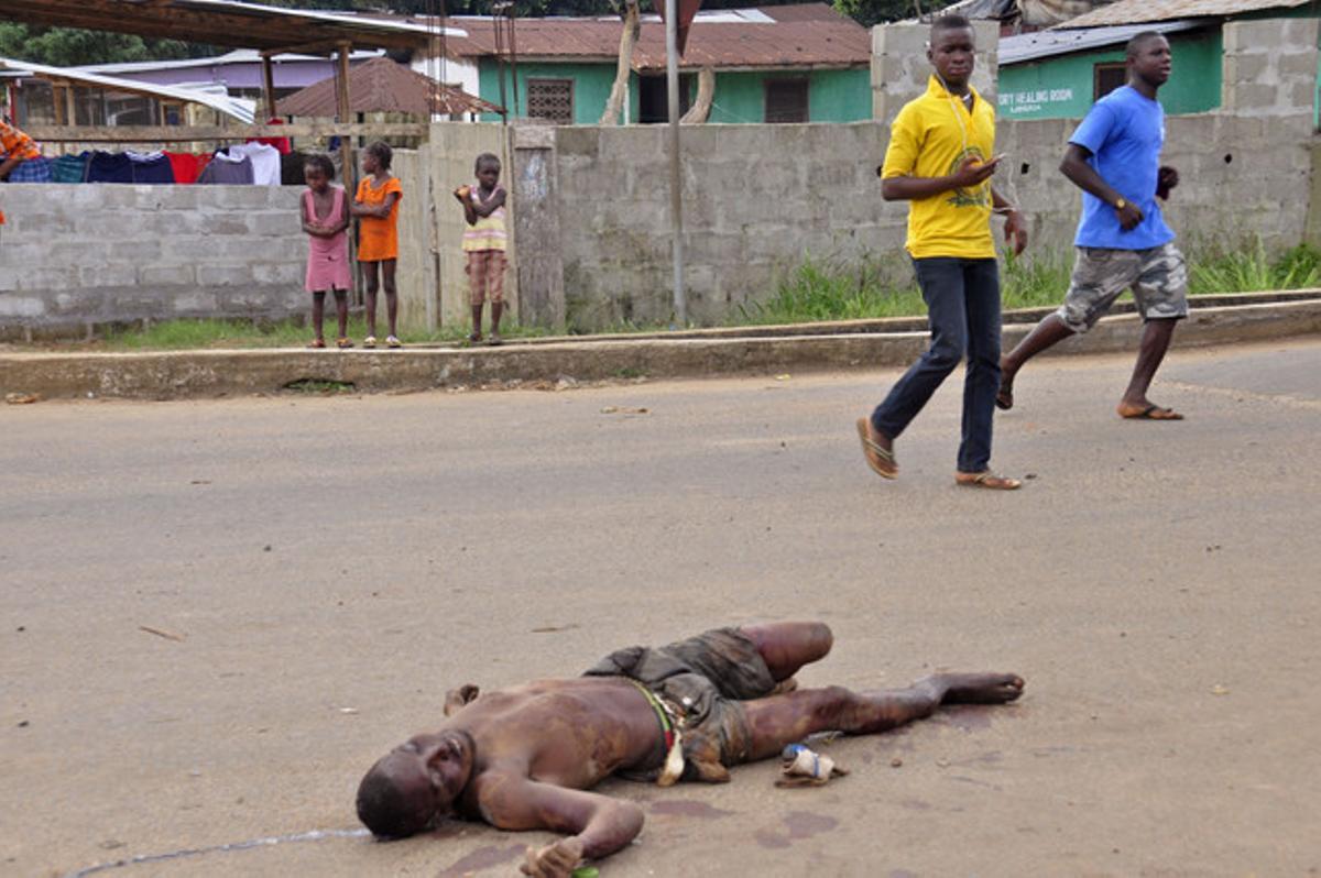 Diversos vianants, davant el cadàver d’un home mort suposadament a causa de l’Ebola, aquest dimarts a Monròvia (Libèria).