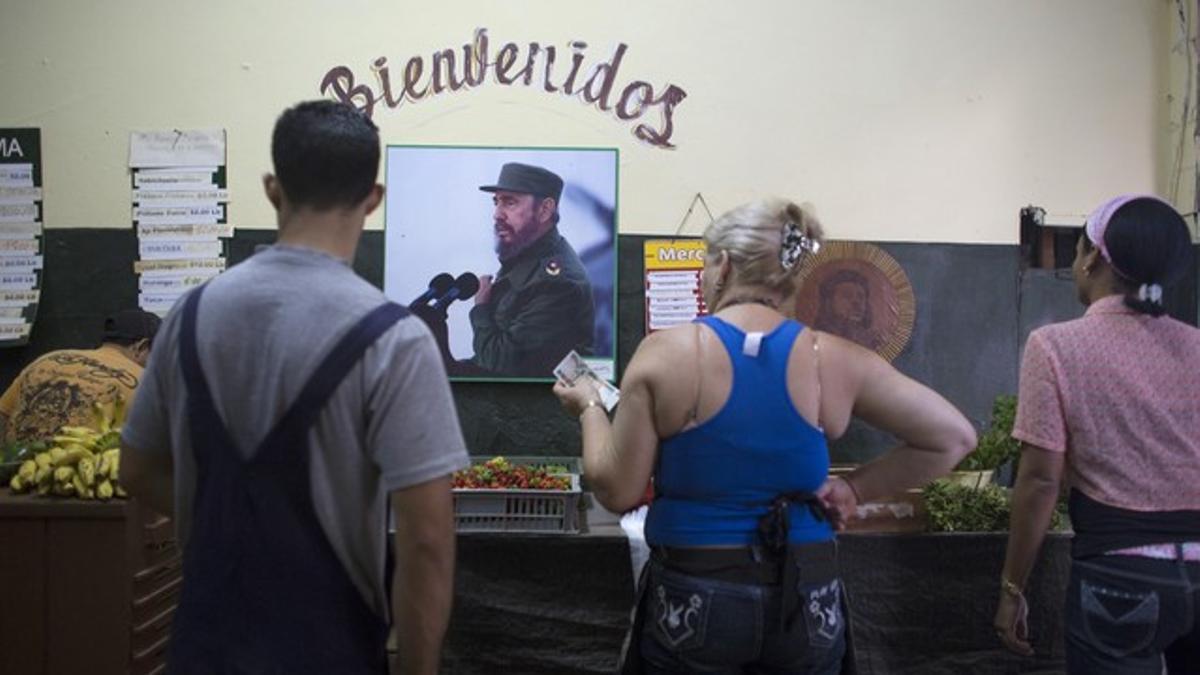 People buy vegetables as a photograph of Cuba's former President Fidel Castro decorates a wall inside a subsidised state store in downtown Havan