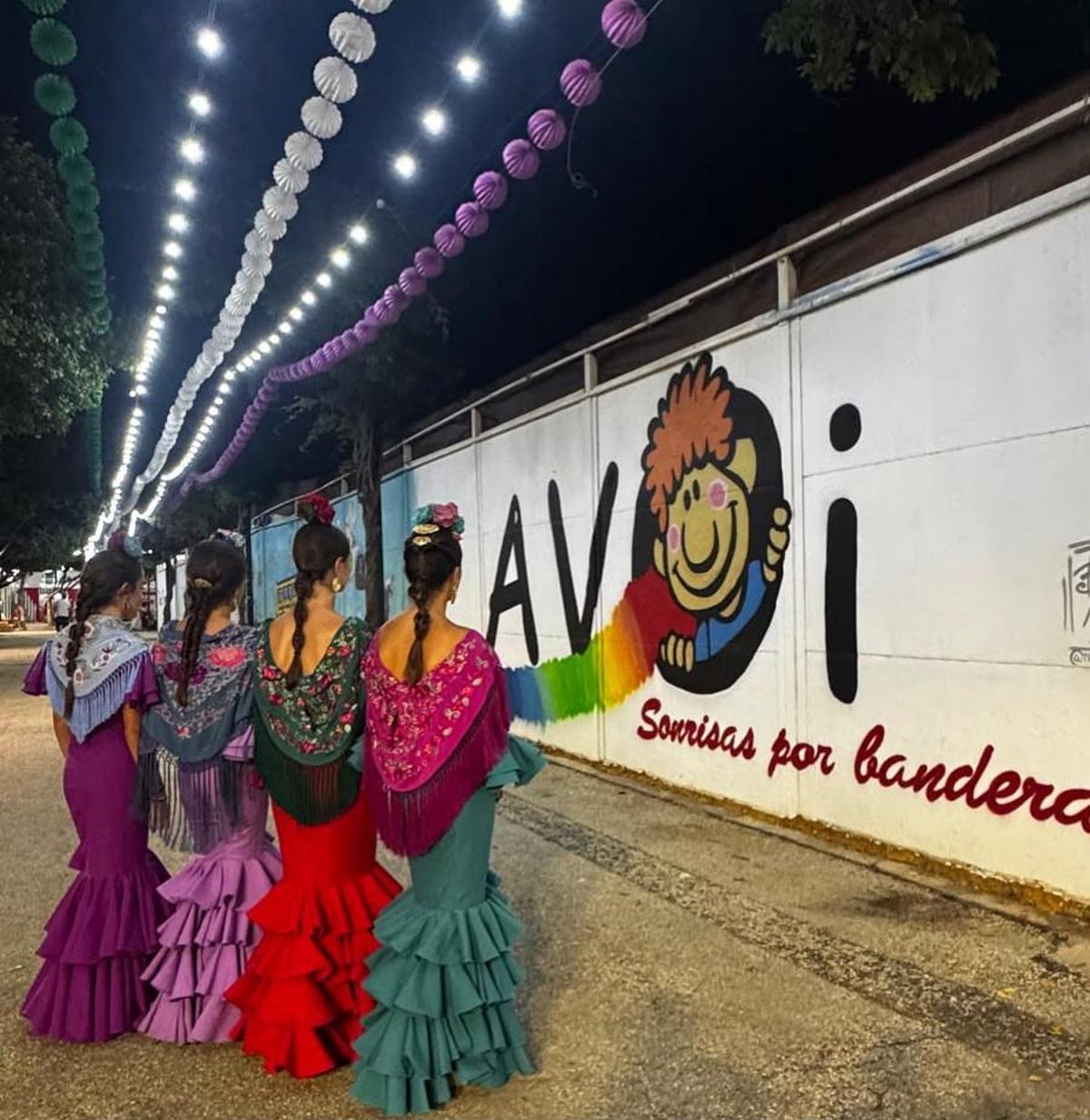 Cuatro mujeres vestidas de gitanas frente a la Caseta AVOI en la Feria de Málaga de 2025.