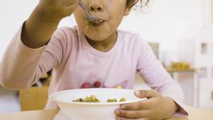 Una niña comiendo en un comedor escolar.