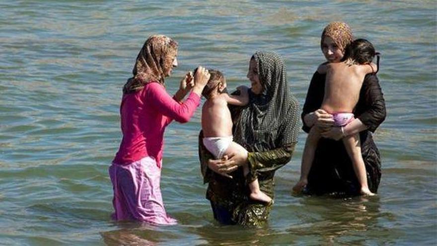 Tres mujeres musulmanas se bañan en el mar vestidas y con velo, en compañía de los pequeños de la familia,                                                           en sus vacaciones.