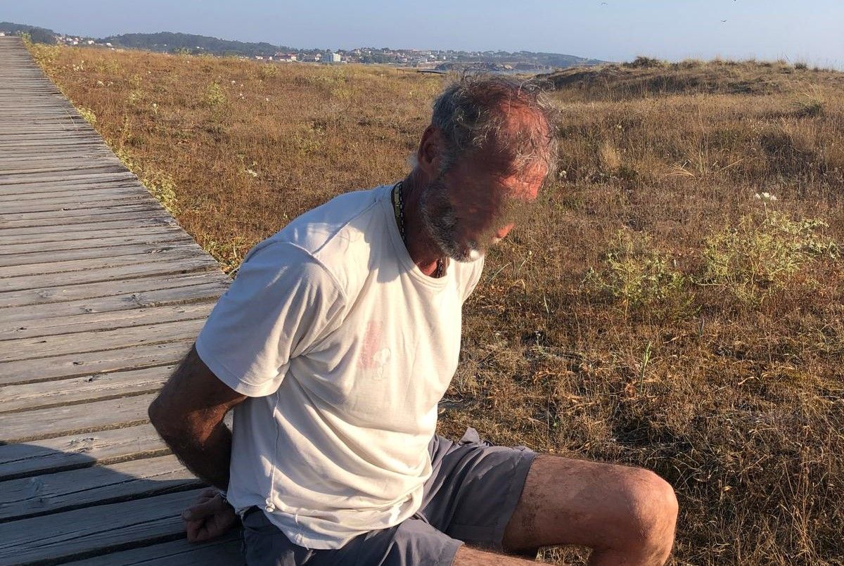 El individuo detenido por la Guardia Civil de O Grove, esposado y sentado en la senda peatonal que atraviesa el istmo de A Lanzada.