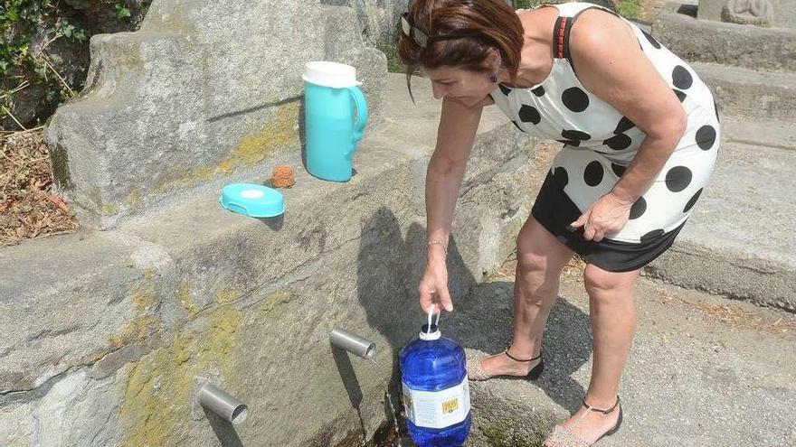 Una mujer coge agua en el manantial de Viñas, en Poio, que está a punto de secar. // Rafa Vázquez