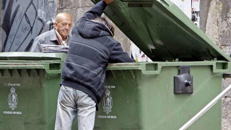 Un hombre rebusca en un contenedor de basura.