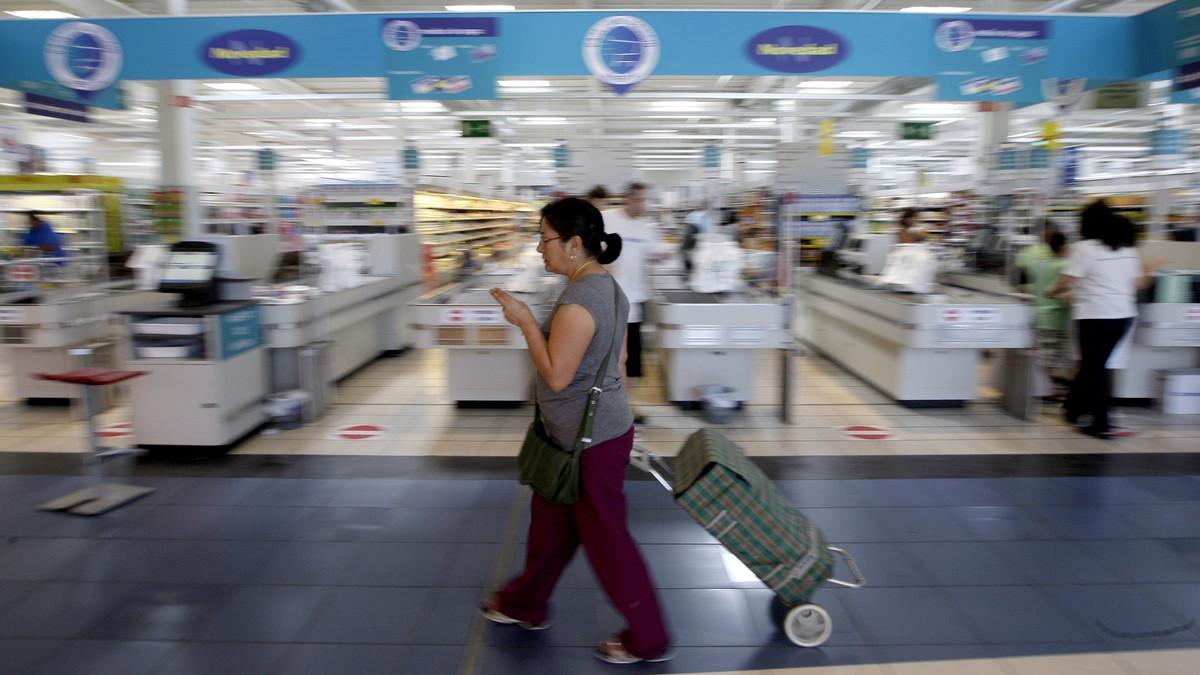 Una mujer camina con su carro de la compra ante la entrada de un hipermercado.