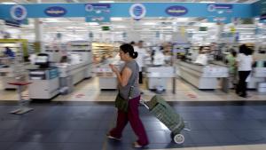 Una mujer camina con su carro de la compra ante la entrada de un hipermercado. 