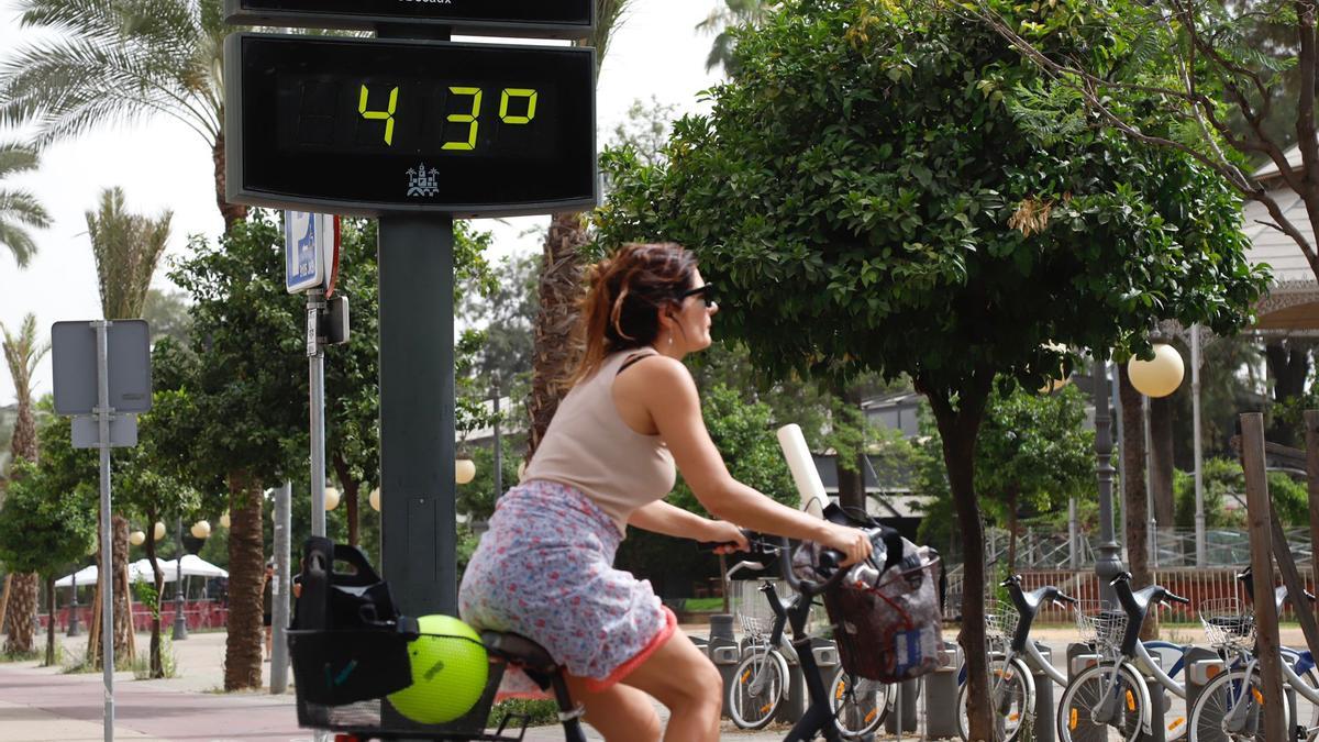 Una mujer pasa con su bicicleta junto a un termómetro urbano en Córdoba, este martes.