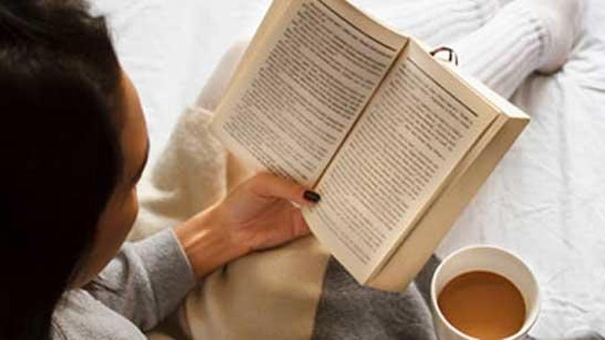 Una mujer lee un libro con un café.