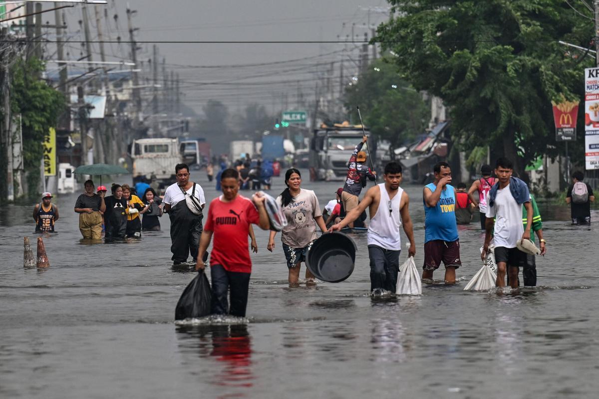 La gente camina a través de una calle inundada después de las fuertes lluvias traídas por el monzón del suroeste en Pampanga el 31 de agosto de 2026. (Foto de Jam STA ROSA / AFP)