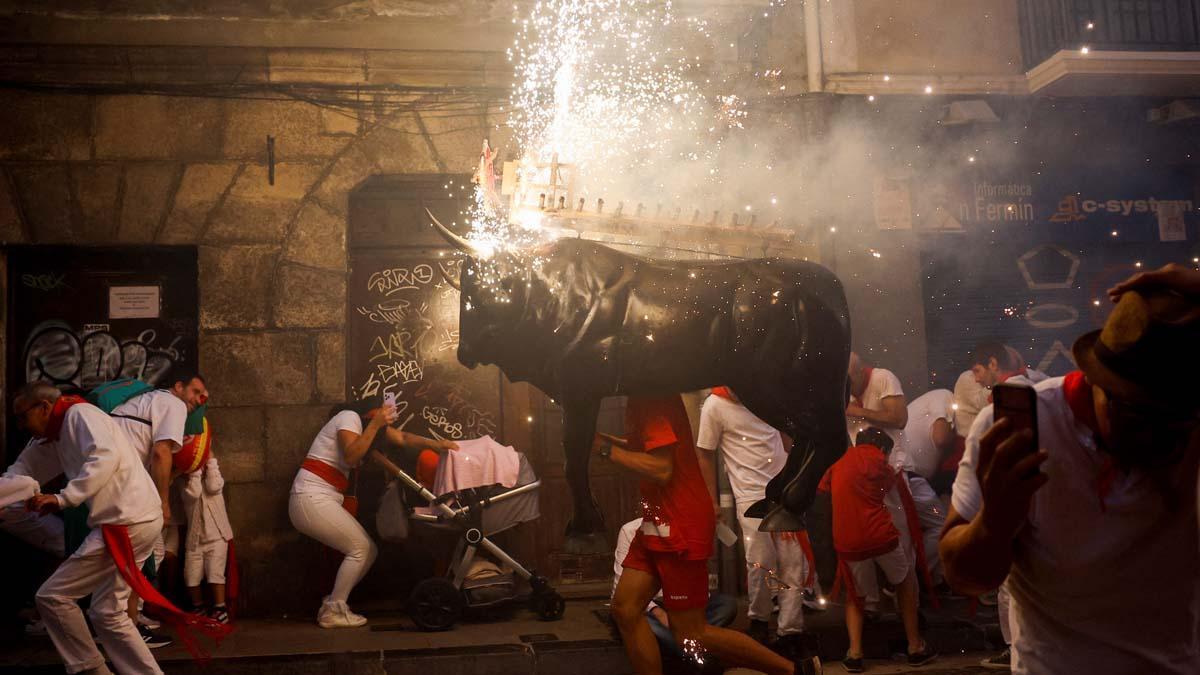 Los juerguistas reaccionan junto al Toro de Fuego, un hombre que lleva una figura de toro llena de fuegos artificiales, durante el festival de San Fermín en Pamplona.