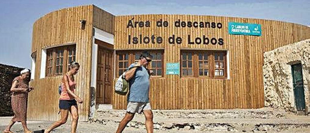 Tres personas caminan por delante del Área de Descanso del islote de Lobos.