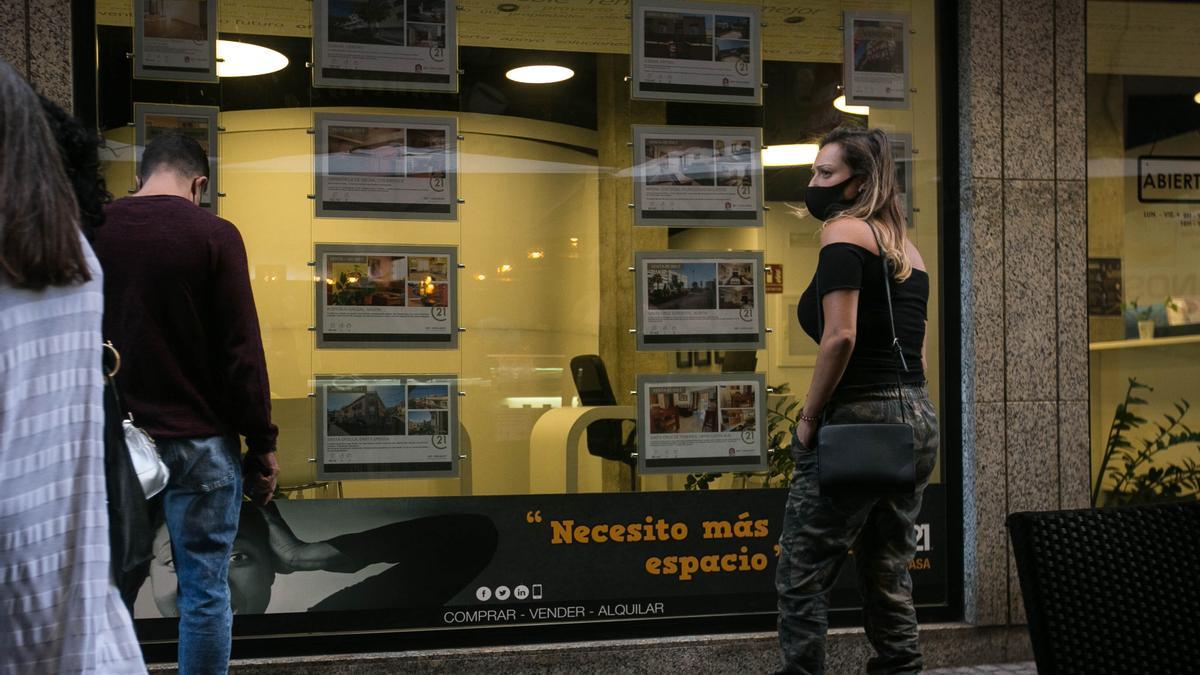 Un hombre y una mujer miran los anuncios de viviendas en alquiler en el escaparate de una inmobiliaria.
