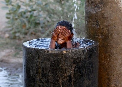 A girl bathes to cool off herself with water that is leaking from a broken pipe valve on a hot summer day on outskirts of Ahmedabad