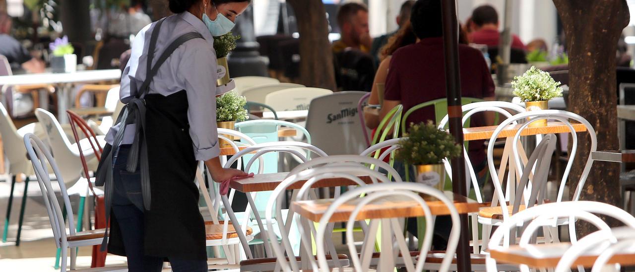 Una camarera limpia unas mesas en la terraza de un restaurante.