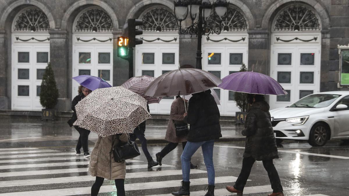 Varias personas se protegen de la lluvia este lunes en una calle del centro de Oviedo.