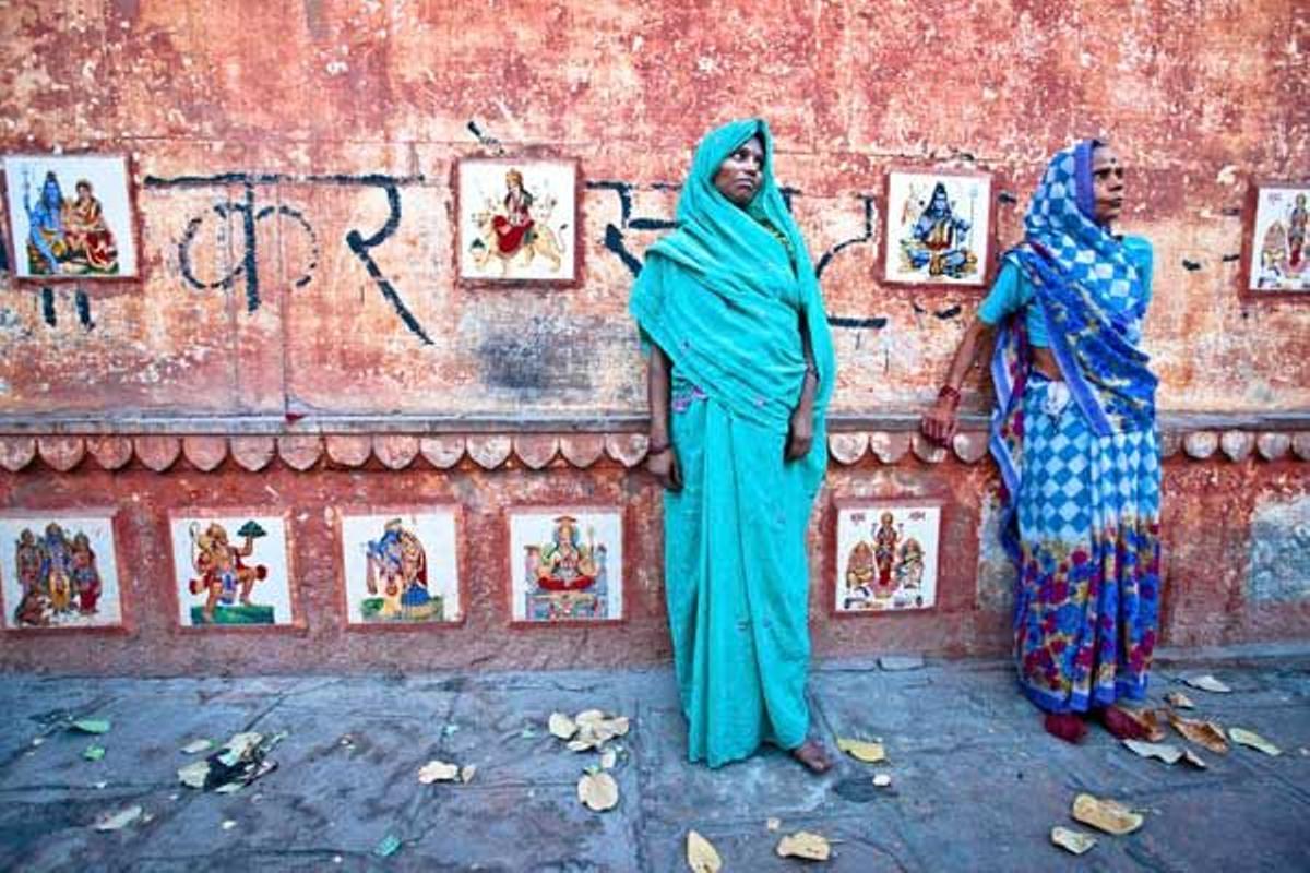 Mujeres vestidas con saris frente a un muro decorado con motivos hinduistas.