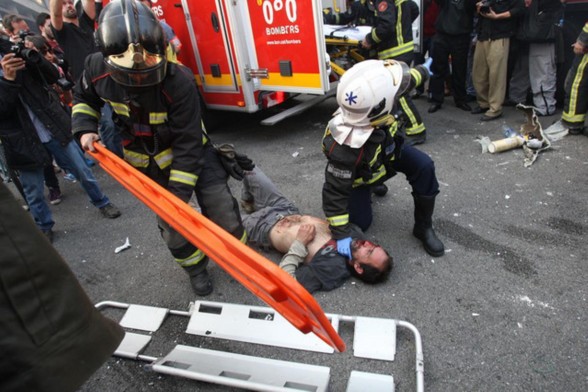 Unos bomberos atienden a un herido en los incidentes tras la manifestación contra la reforma laboral, en Barcelona.