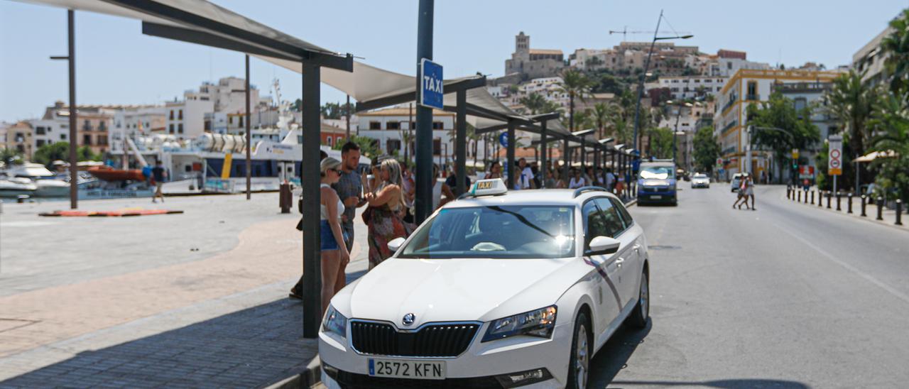 Un taxi en la parada del puerto de Ibiza repleta de gente.