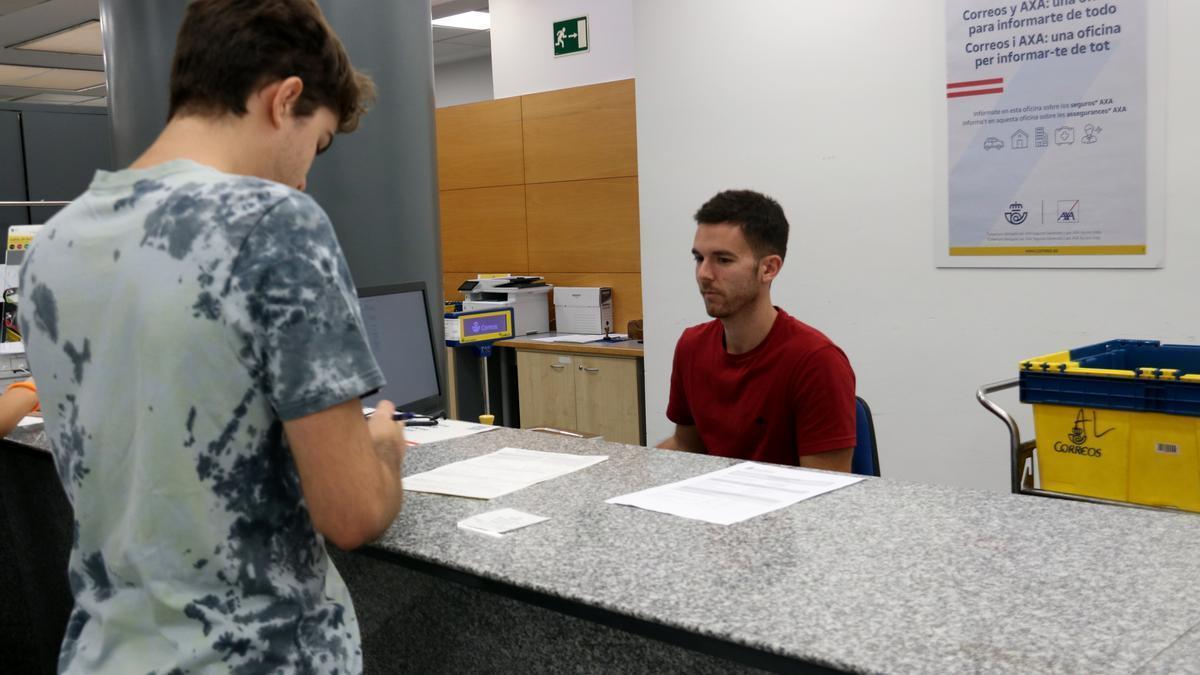 Un treballador de Correus explica el procediment per demanar el vot postal a un ciutadà aquest dissabte. | ACN/GUIFRÉ JORDAN