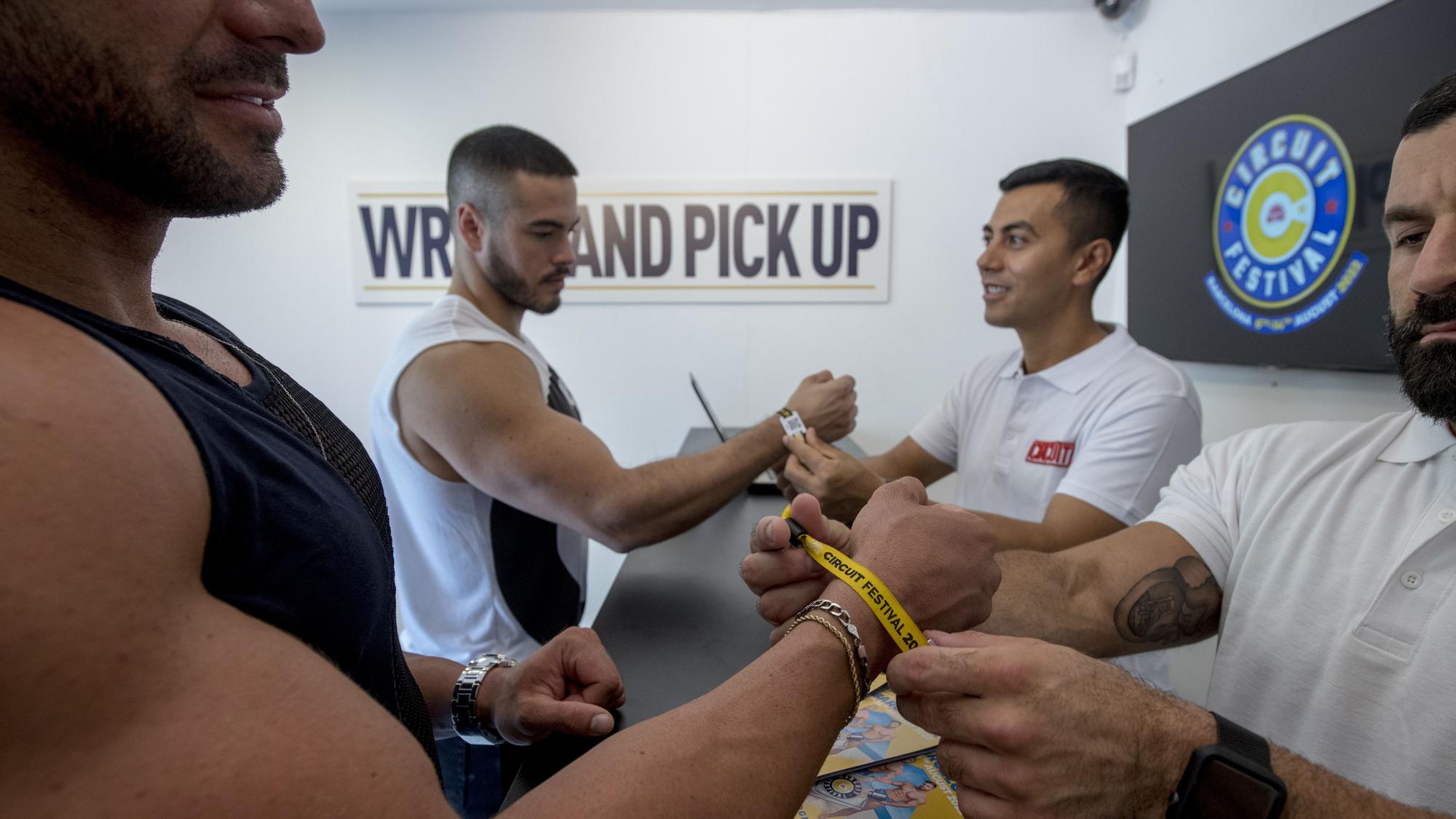 Dos hombres recogen sus correspondientes pulseras para participar en los eventos del festival gay Circuit que inicia sus actividades este sábado.