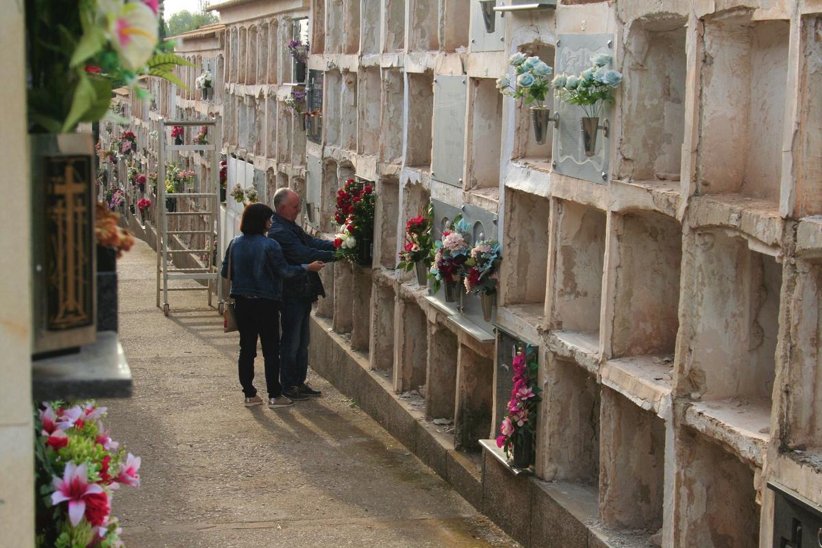 Dos personas colocan flores en un nicho de una de las calles más viejas del cementerio que están siendo vaciadas para derribarlos y construir nuevos pabellones.