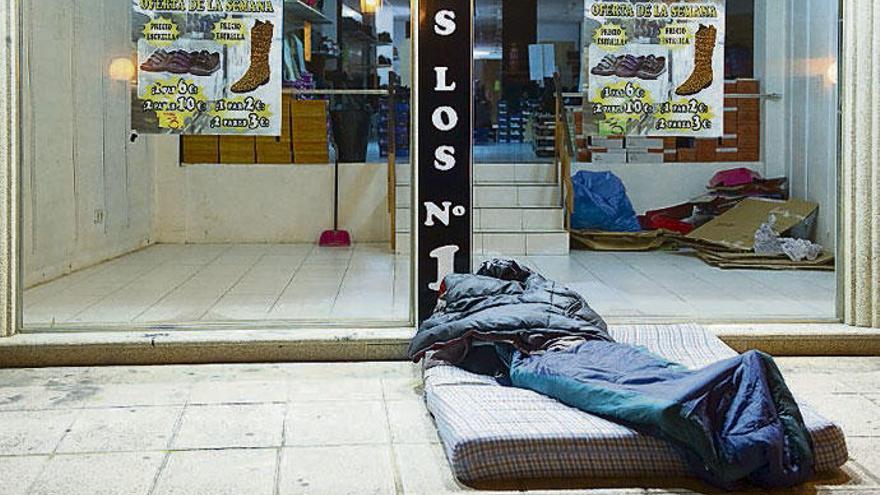 Un &#039;sin techo&#039; duerme en un colchón delante de un comercio.