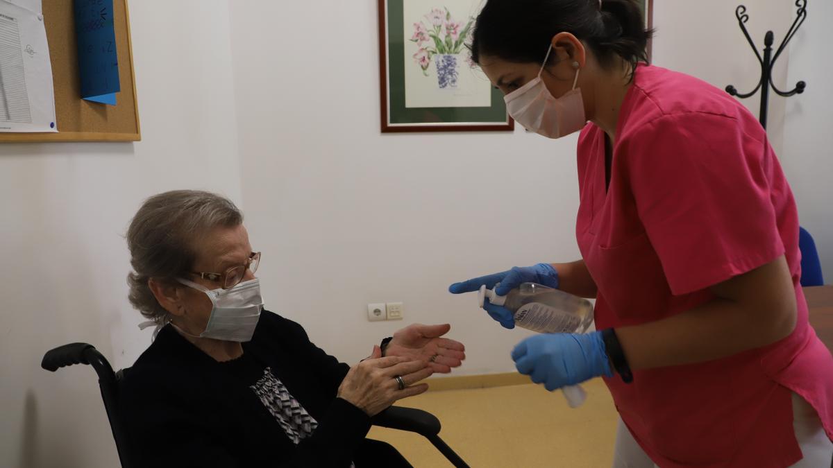 Una trabajadora ofrece gel desinfectante a la usuaria de un geriátrico.