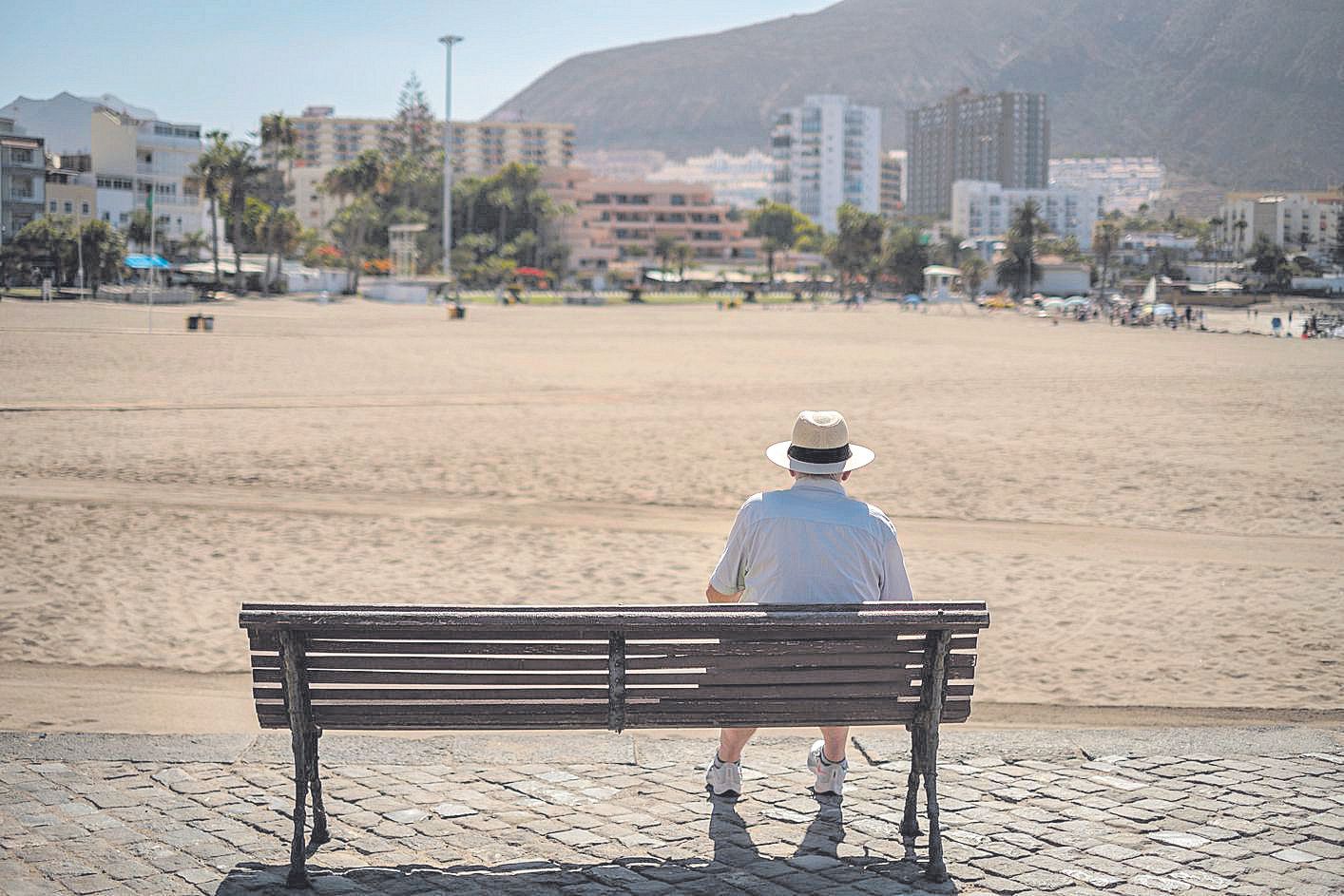 Un hombre mira desde un banco una playa desierta en Los Cristianos, al sur de Tenerife, en lo peor de la pandemia.