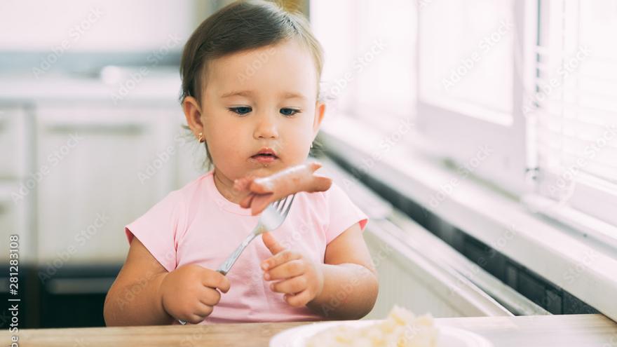 Una niña mira una salchicha.
