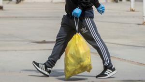 Una persona lleva una bolsa de basura hacia un contenedor, en una imagen de archivo.