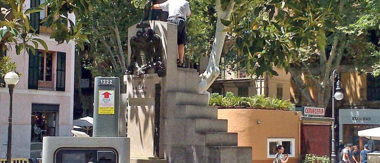 Un turista, encaramado a la estatua de Antoni Maura para hacerse una foto.