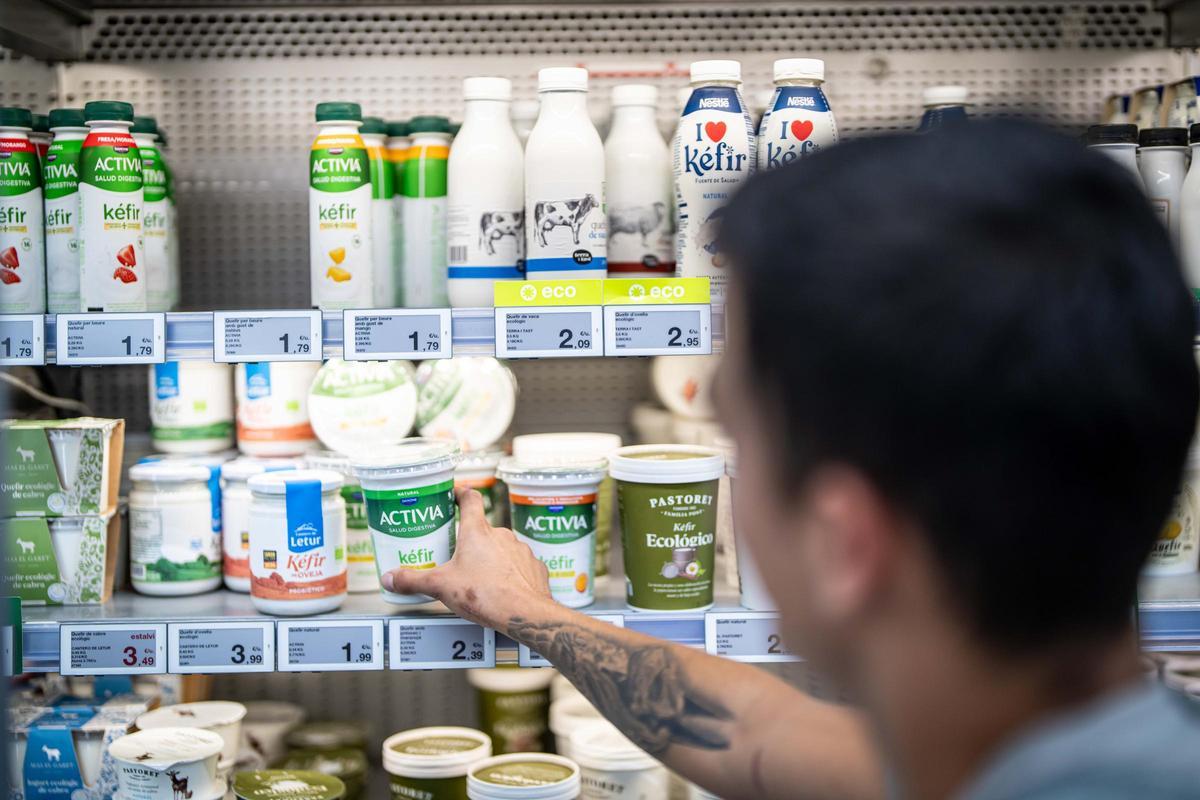 Un hombre escoge un kéfir de una nevera de productos lácteos de un supermercado