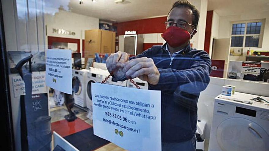 Pablo Pedraz coloca un cartel para avisos en su tienda de electrodomésticos de Avilés. | Ángel González