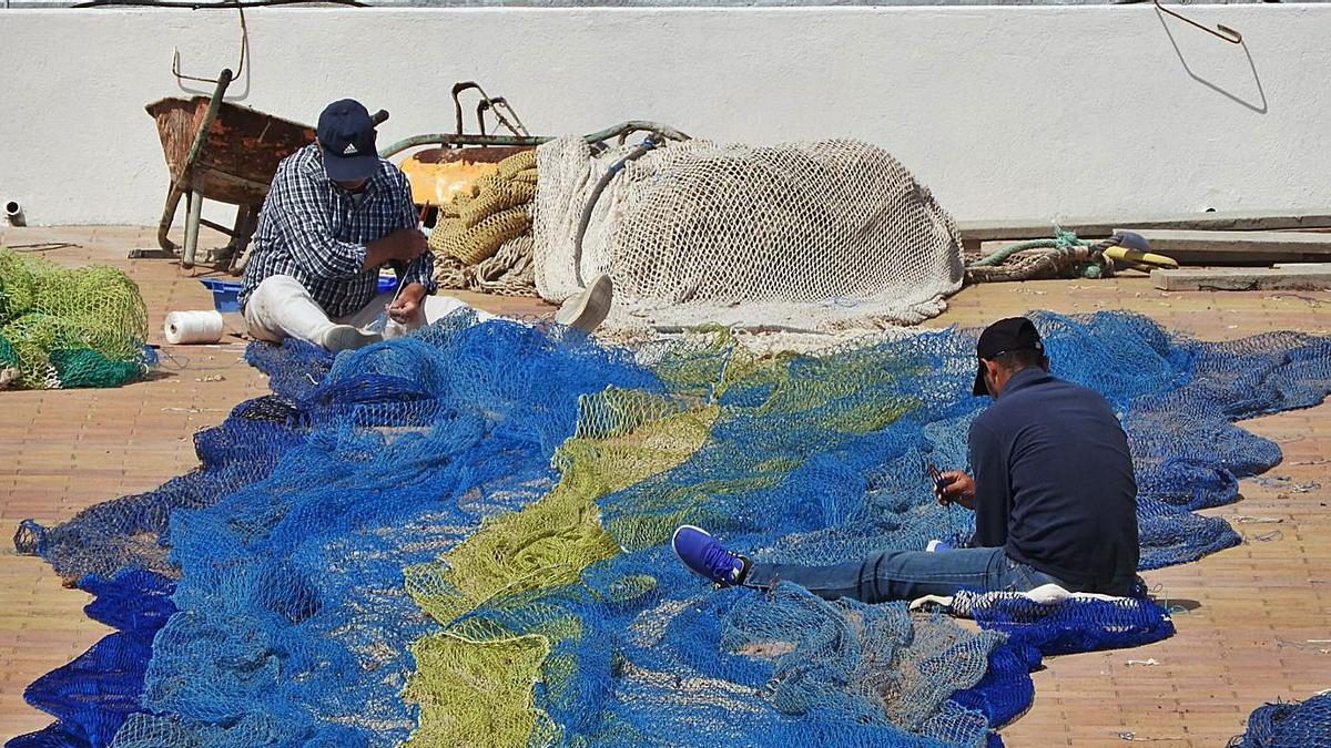 Dos pescadores remiendan redes en la explanada del puerto de la Savina.