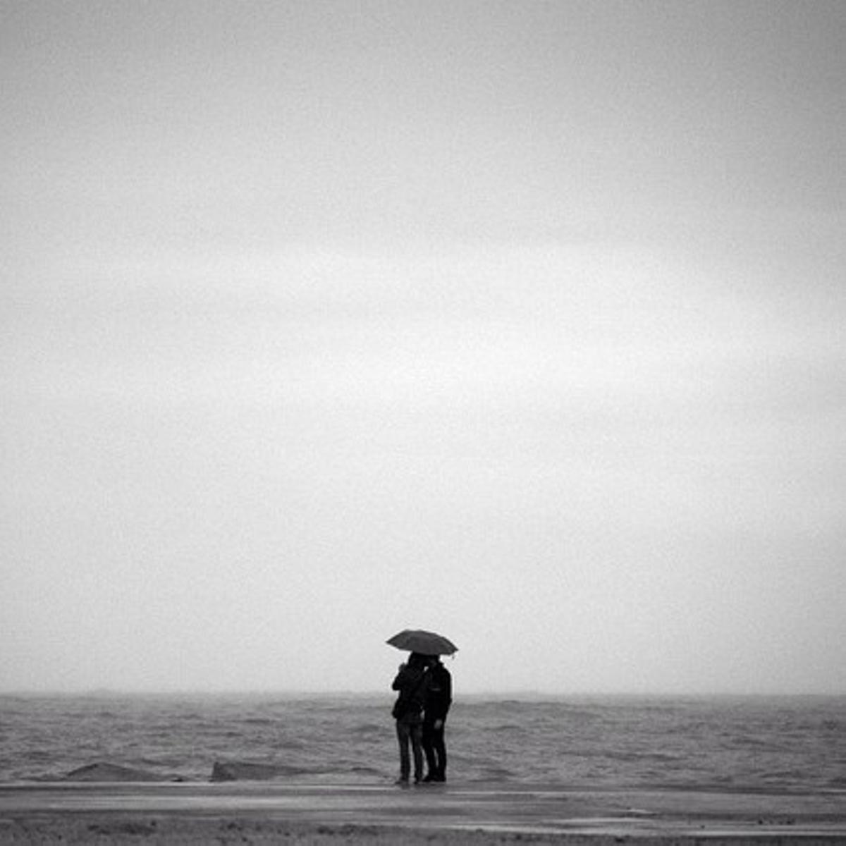 Una pareja mira el mar bajo un paraguas.