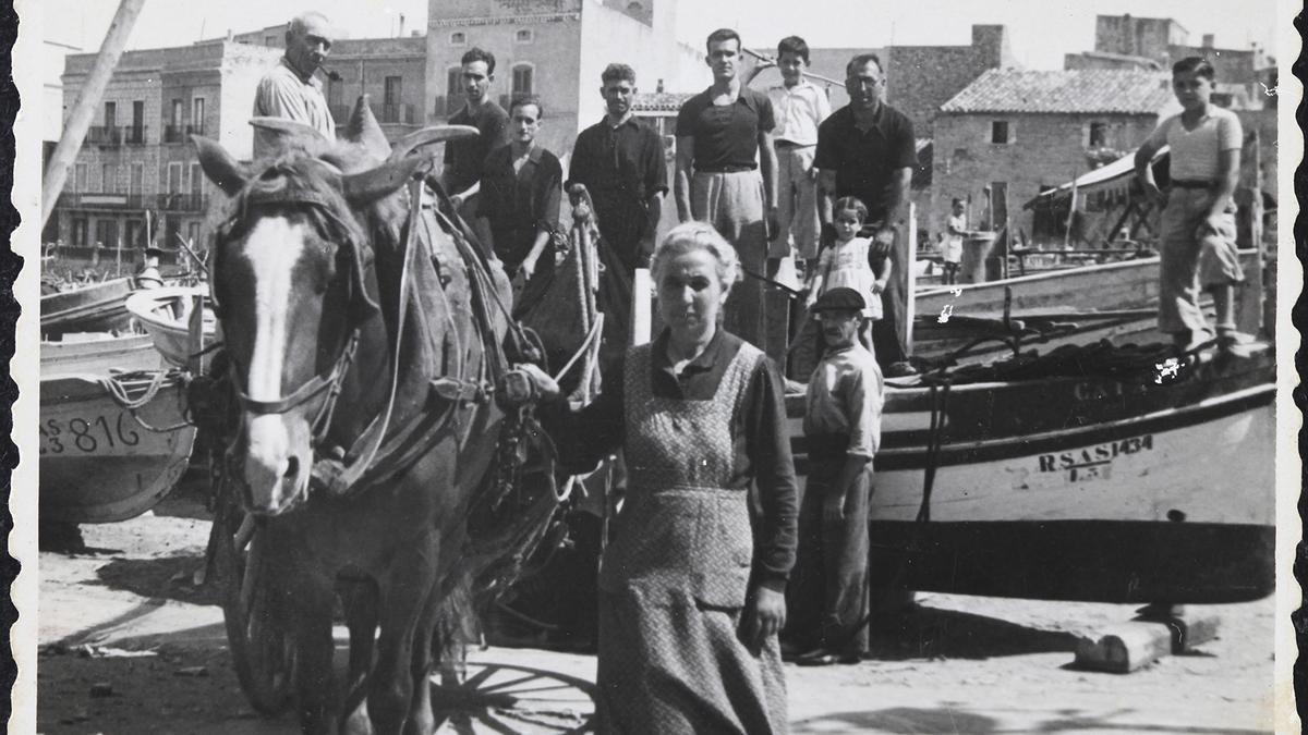 En primer terme, la Caterina de Can Guinya amb el cavall i el carro d’en Quildo, amb els quals transportava les xarxes de pesca de la platja als estenedors, per assecar-les i remendar-les, als anys 30.