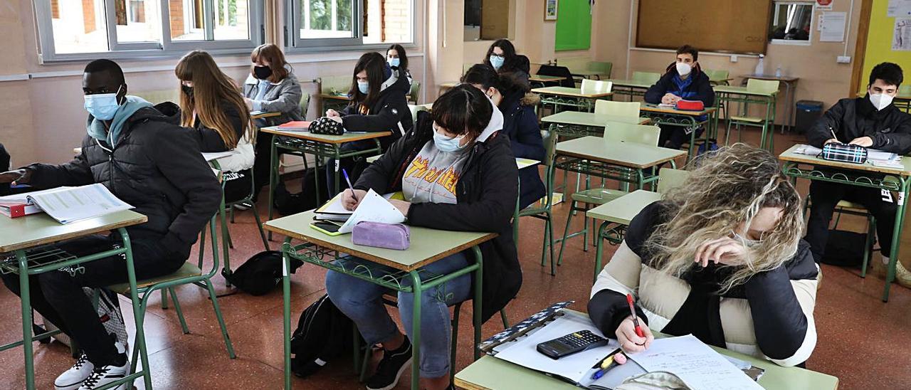 Alumnos del Instituto Padre Feijoo de Gijón, este viernes, en clase, con abrigos para combatir el frío que entra por las ventanas, abiertas para reducir el riesgo de contagio por covid. | Juan Plaza