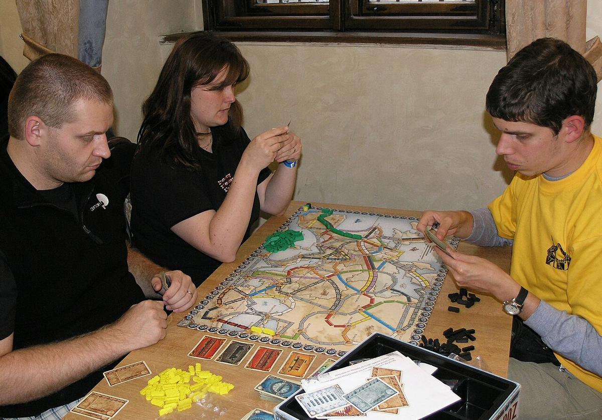 Varias personas juegan al Ticket to Ride, también conocido como Aventureros al tren.
