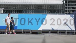 Ciudadanos en Japón caminan junto a un cartel de los Juegos Olímpicos de Tokio 2020