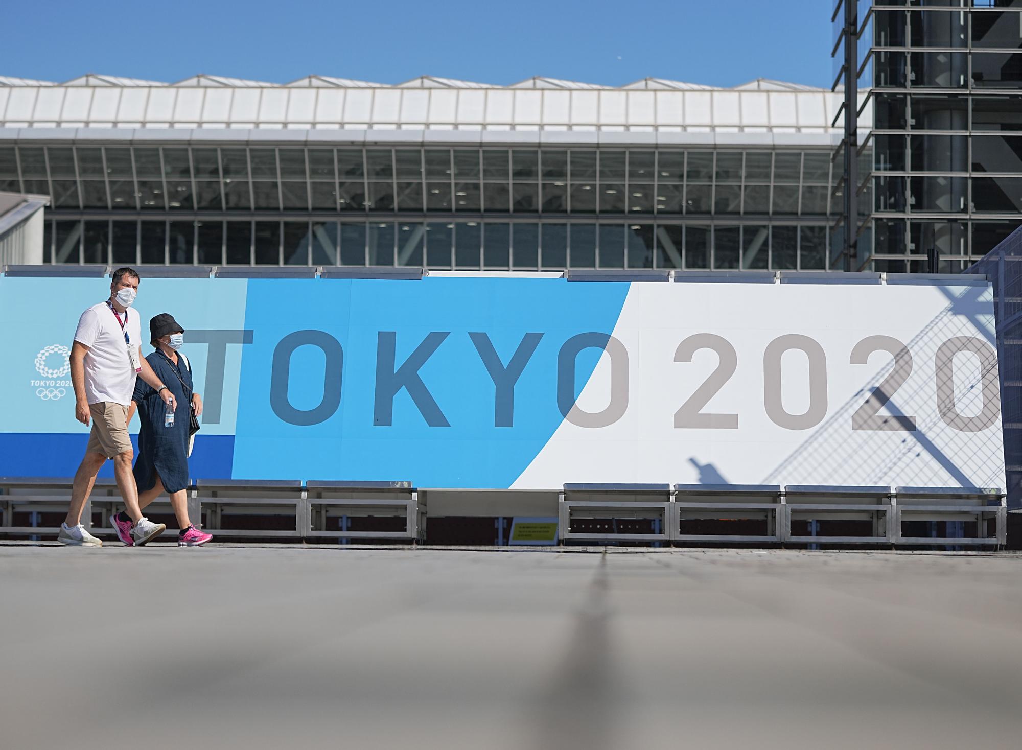 Ciudadanos en Japón caminan junto a un cartel de los Juegos Olímpicos de Tokio 2020