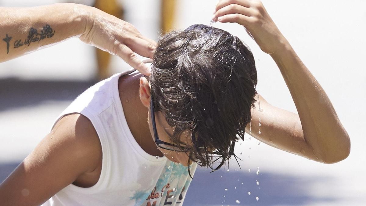 Un niño se echa agua por la cabeza para refrescarse.