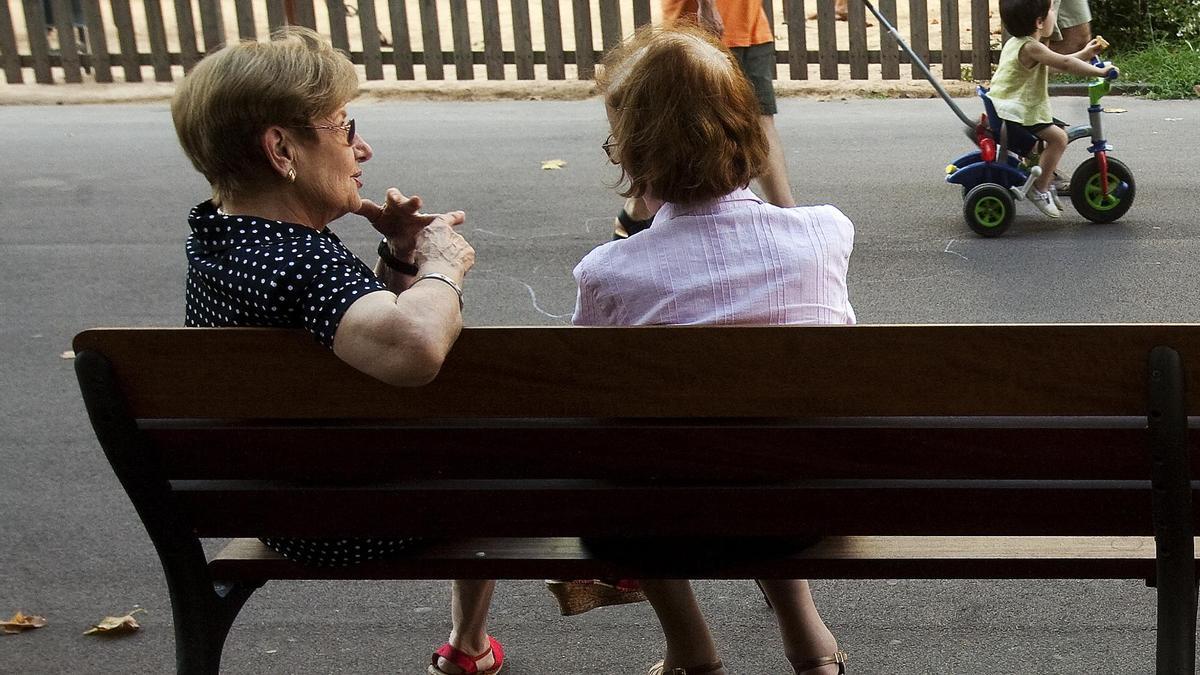 Dos mujeres jubiladas conversan sentadas en el banco de un parque.