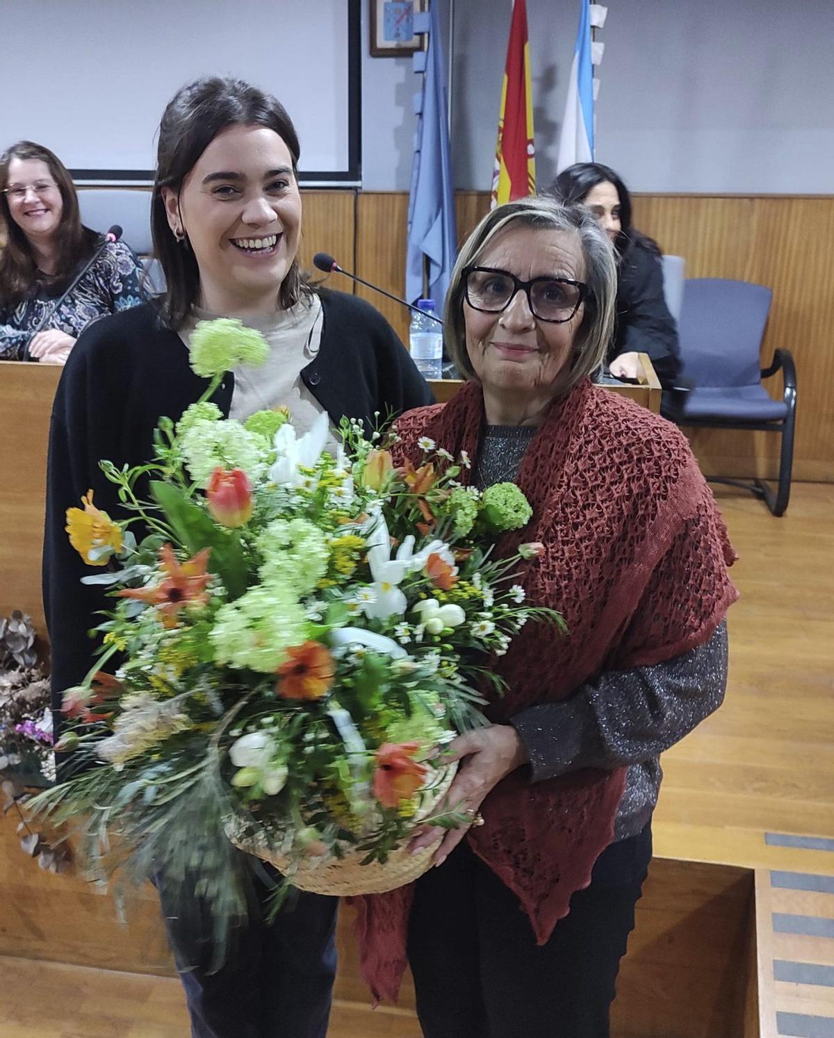 La edil Xiana Abal (BNG) entrega un ramo de flores a su compañera de gobierno Aurora Prieto (EU).